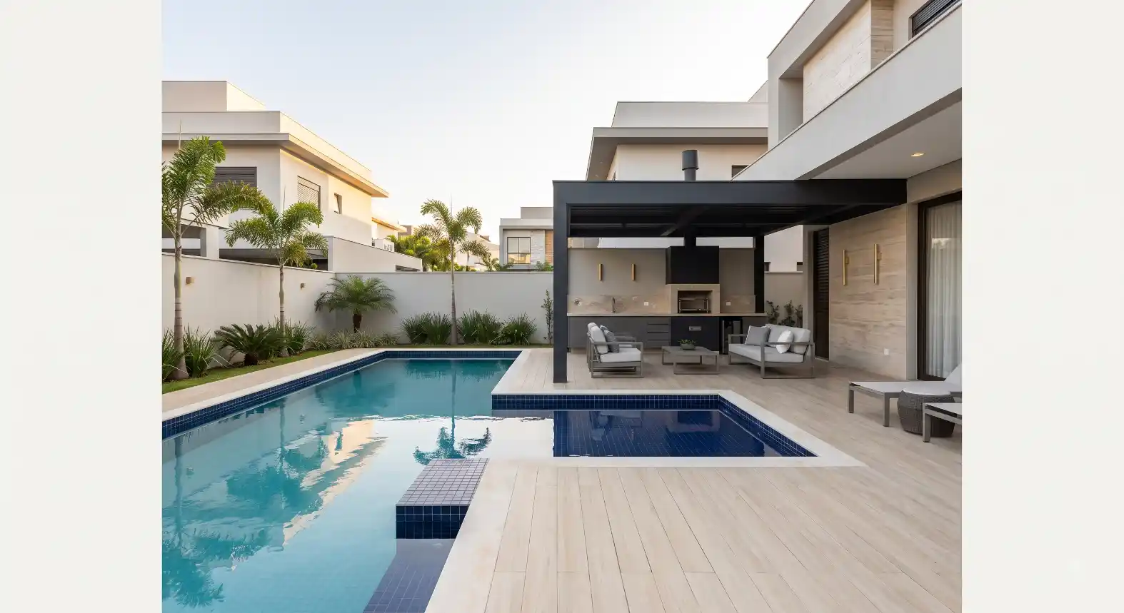 Área externa de casa moderna com piscina retangular azul, deck de madeira e iluminação no quintal, ao lado de churrasqueira com área gourmet e sofás, em projeto residencial